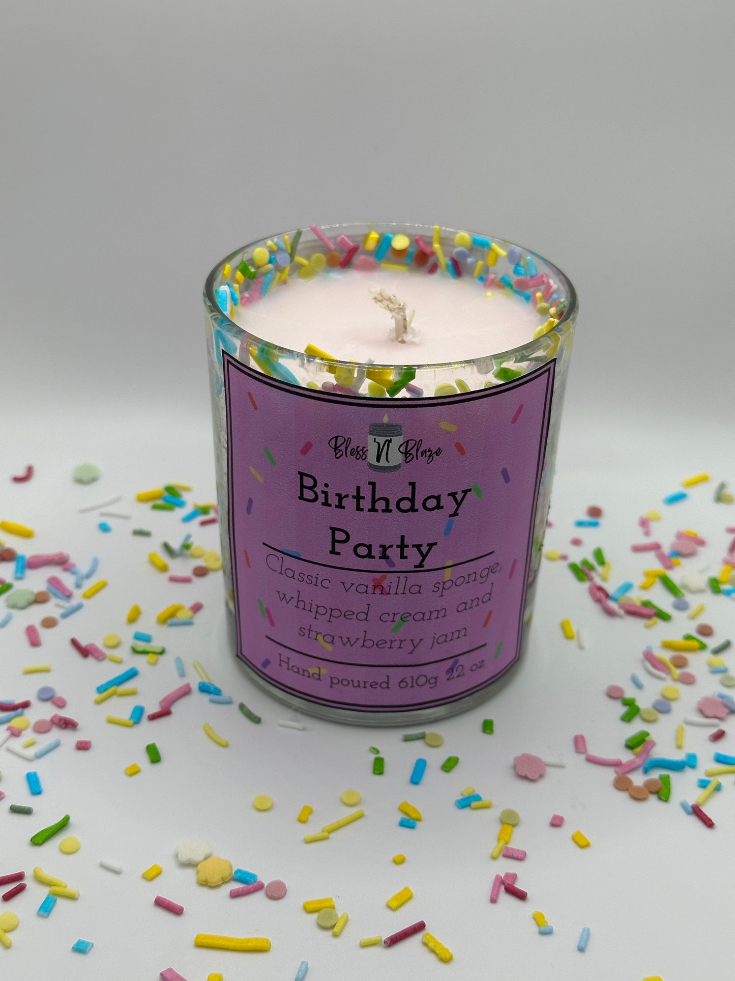 Candle in a container with a pink label on a white background with colorful sprinkles.